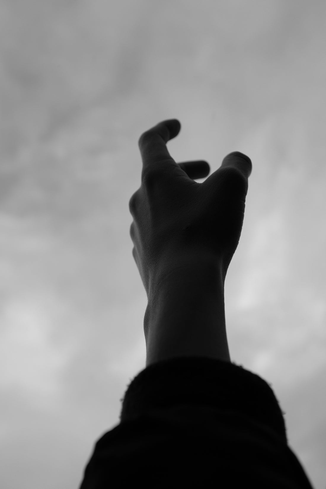 A hand reaching up towards a cloudy sky